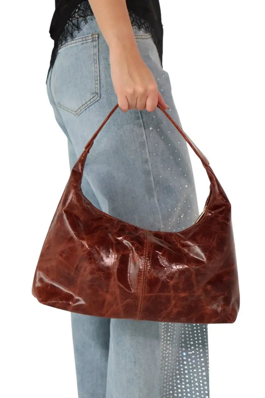 Bolso marrón de cuero sostenido por mujer con jeans claros y blusa negra