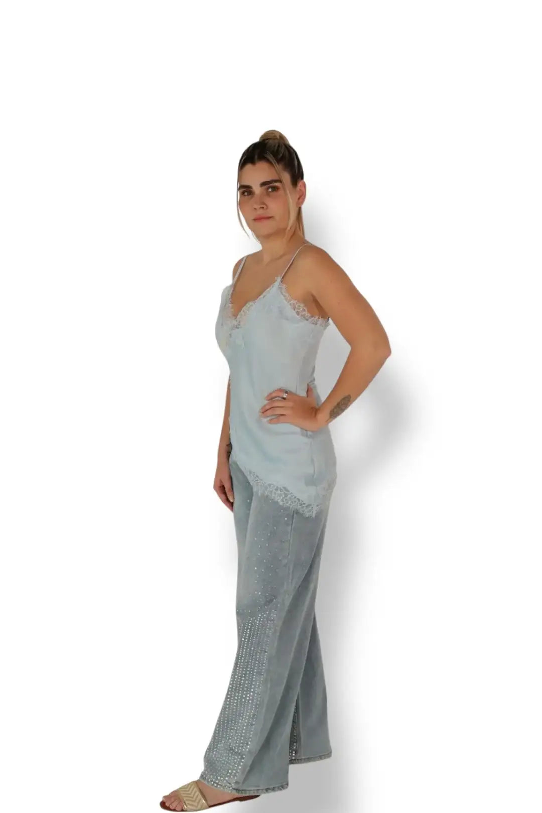 Mujer con blusa de tirantes azul claro y pantalón de mezclilla con pedrería, fondo blanco