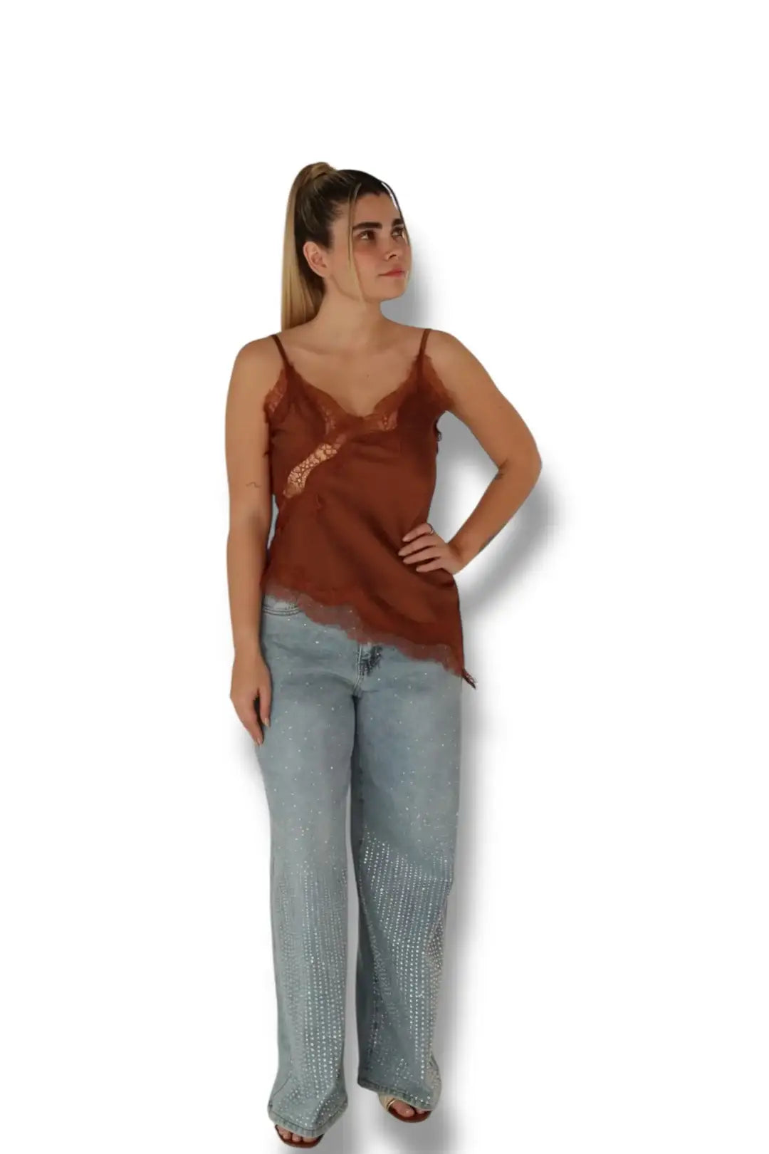 Mujer con blusa lencera marrón y jeans de mezclilla claros con pedrería, fondo blanco.
