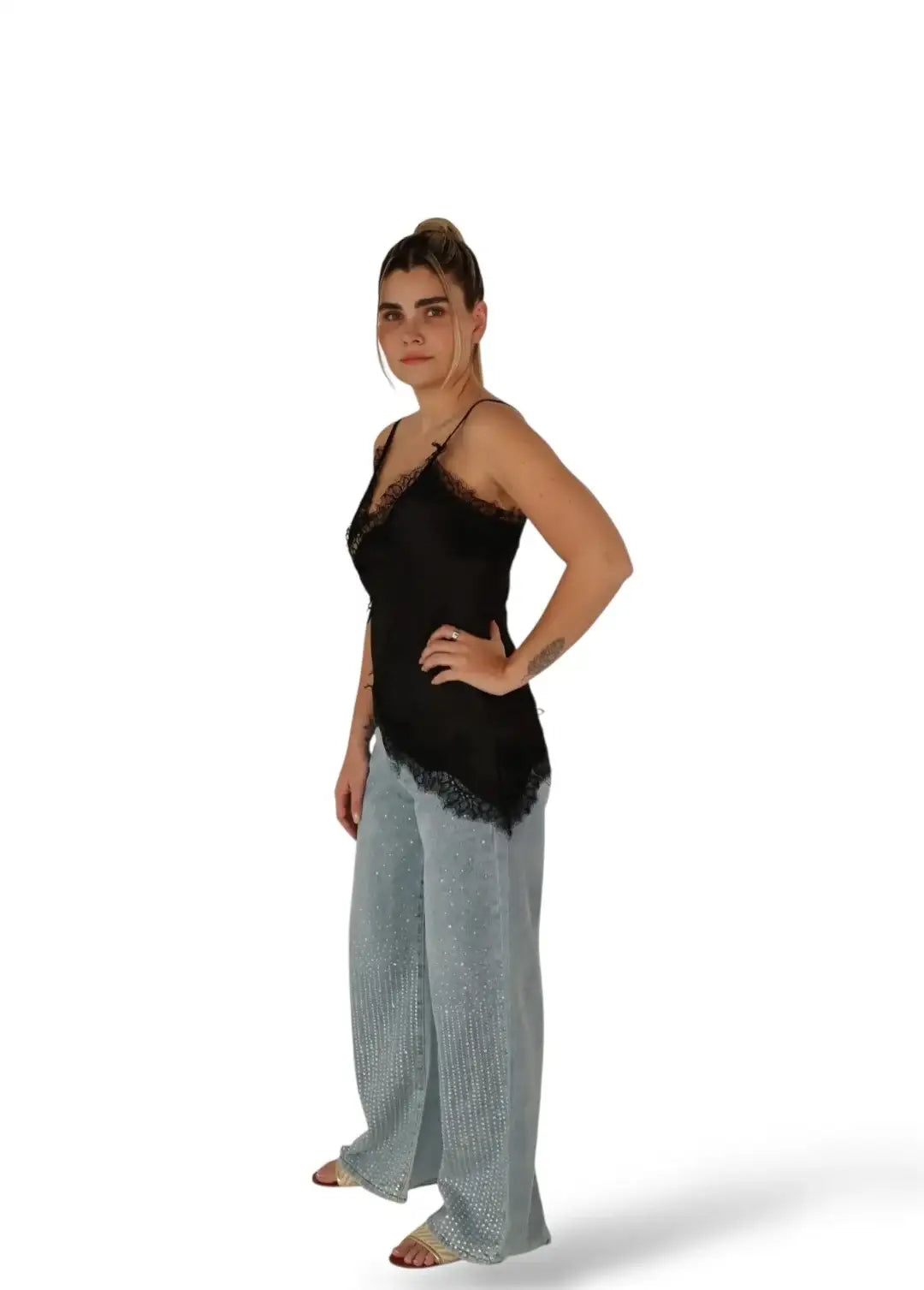 Mujer con top negro de encaje y pantalón amplio de mezclilla con perlas, fondo blanco.