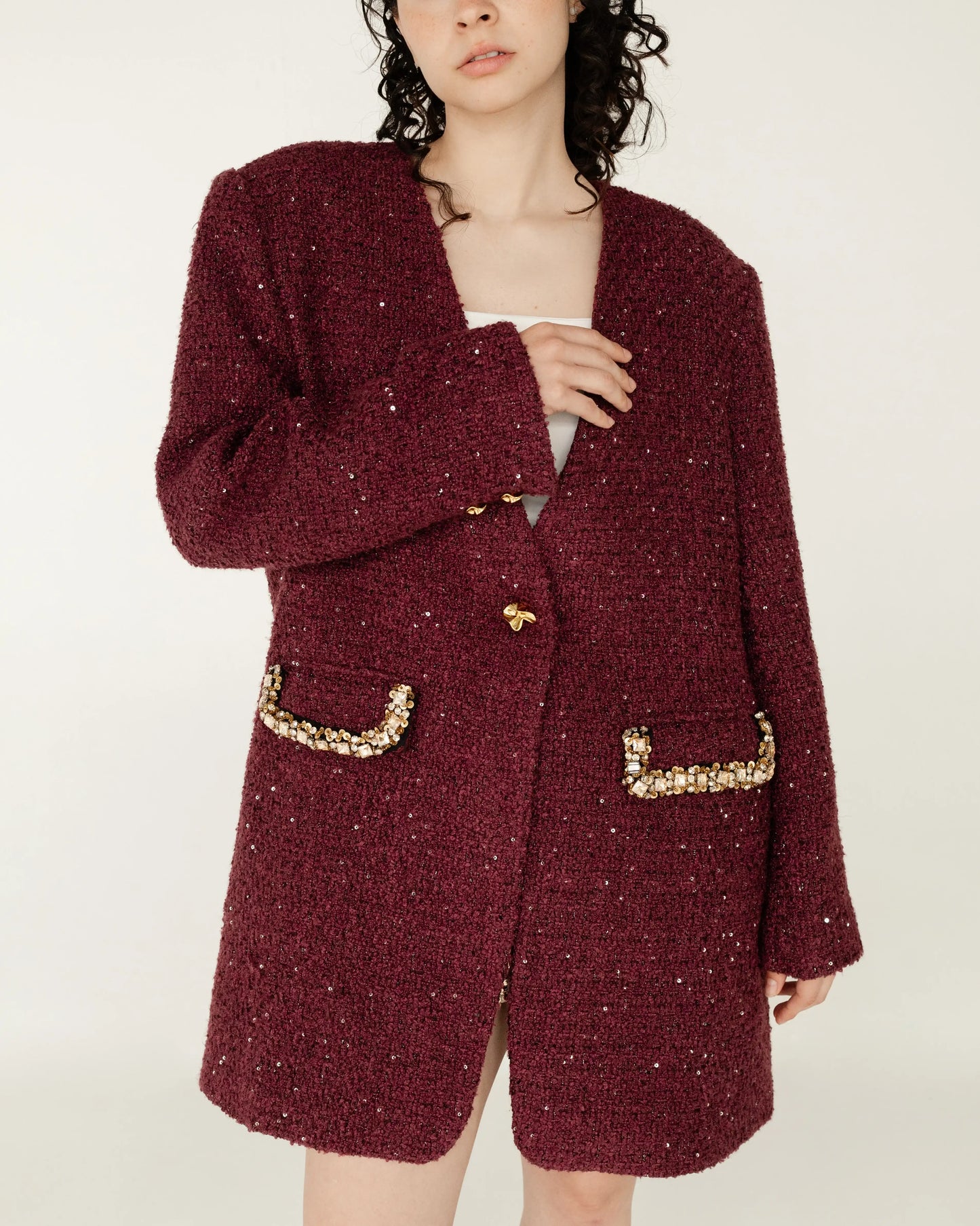 Mujer con saco largo burdeos de textura bouclé, detalles dorados y lentejuelas