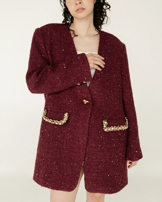 Mujer con saco largo burdeos de textura bouclé, detalles dorados y lentejuelas