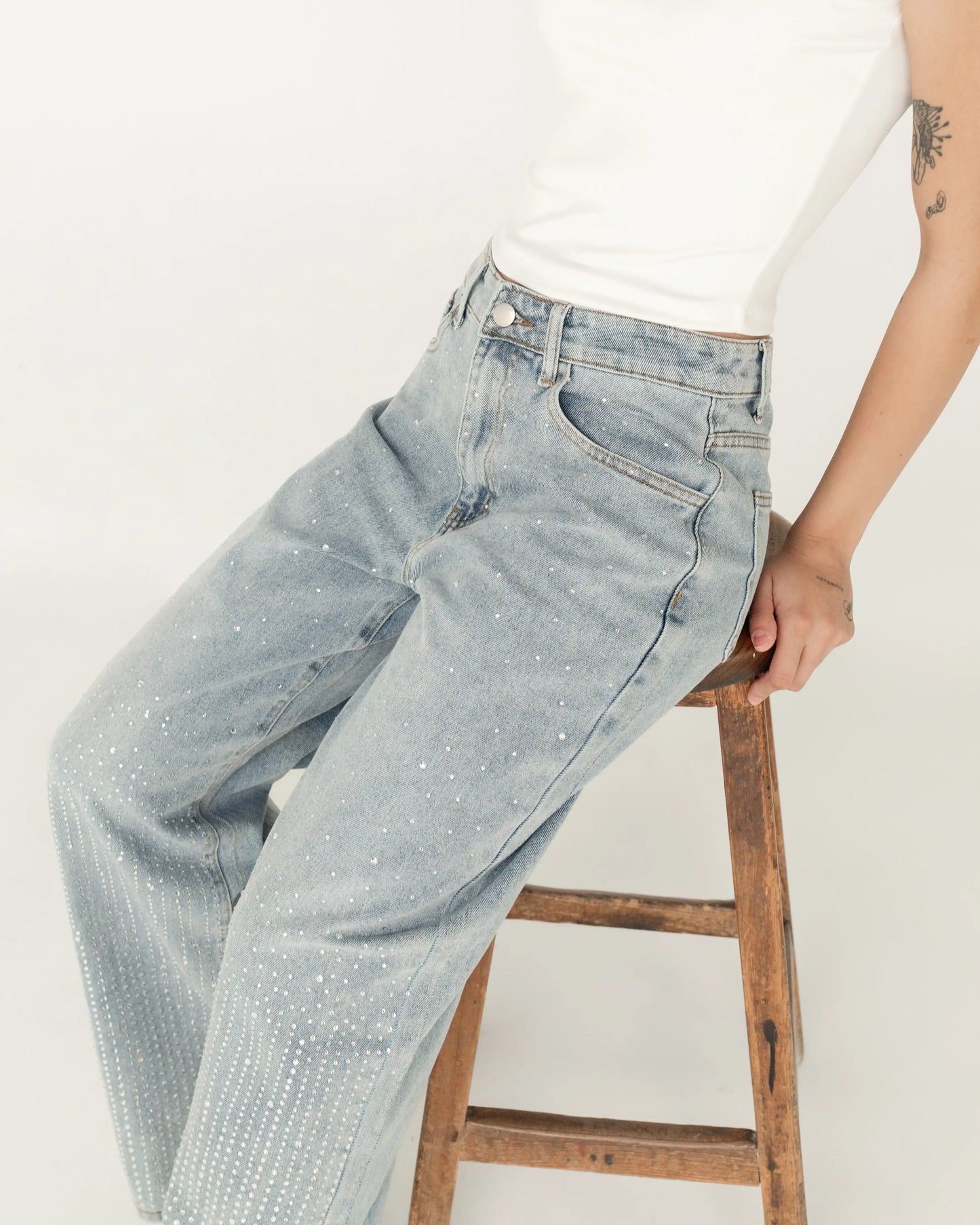 Jeans de mezclilla azul claro con pedrería, mujer sentada en banco, estilo moderno