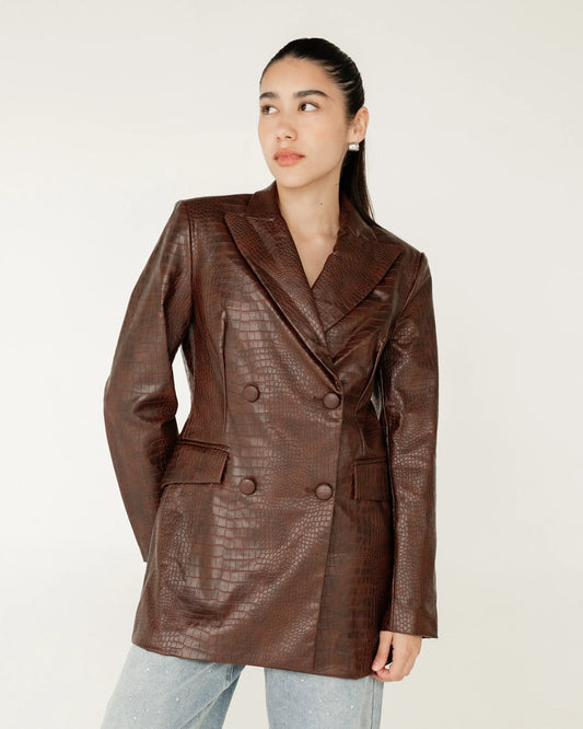 Mujer vistiendo saco marrón tipo piel con textura croco y jeans claros, fondo neutro