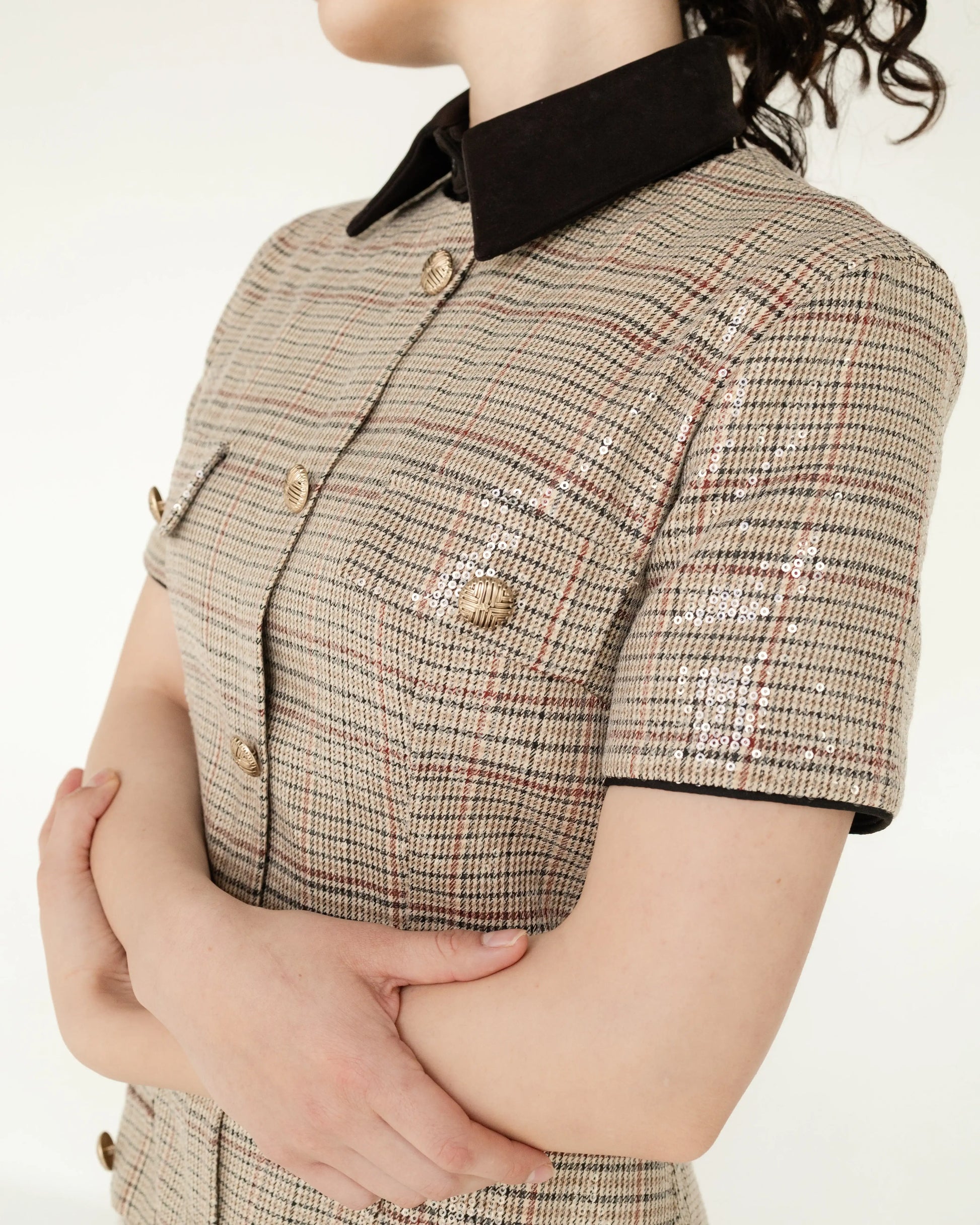 Blusa de cuadros estilo sastre con botones dorados y lentejuelas, mujer de brazos cruzados