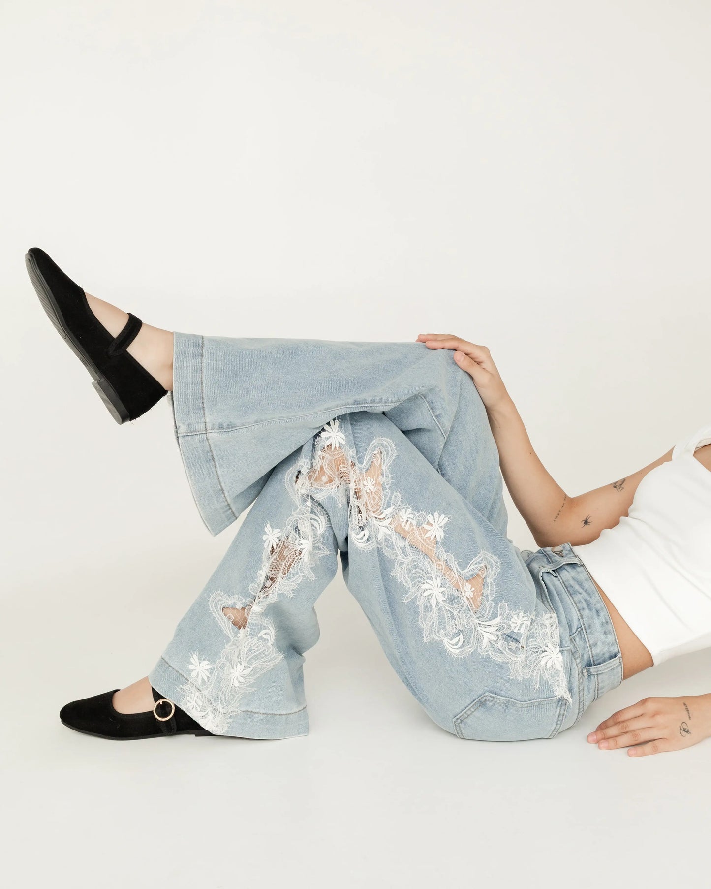 Jeans acampanados azul claro con encaje blanco floral, modelo sentada en fondo blanco