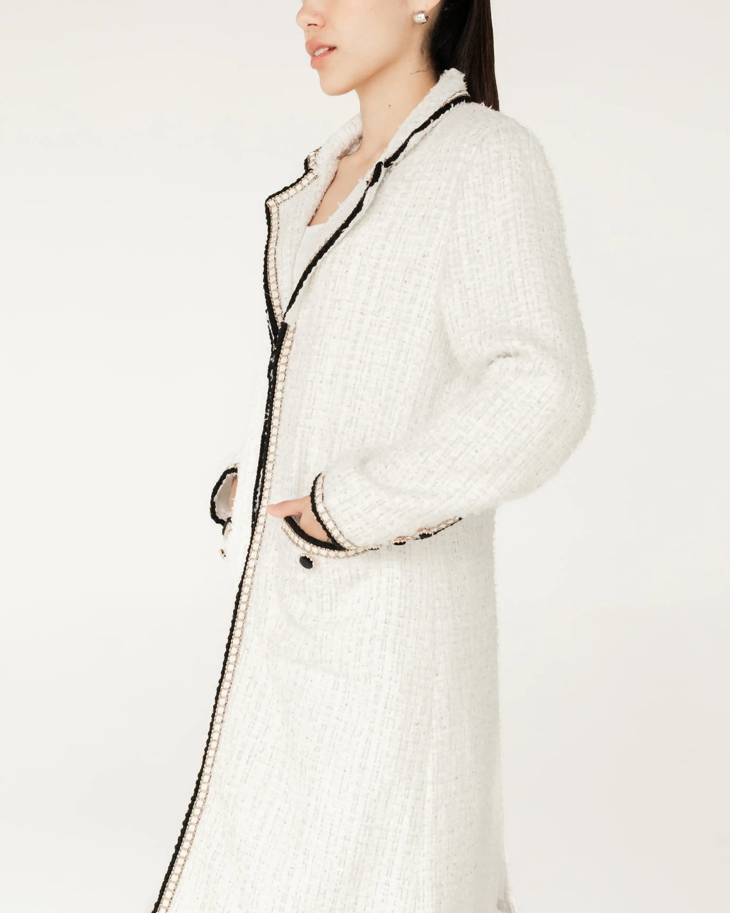 Mujer con abrigo largo blanco de tweed con detalles negros, moda elegante minimalista.