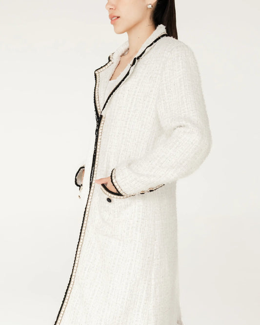 Mujer con abrigo largo blanco de tweed con detalles negros, moda elegante minimalista.