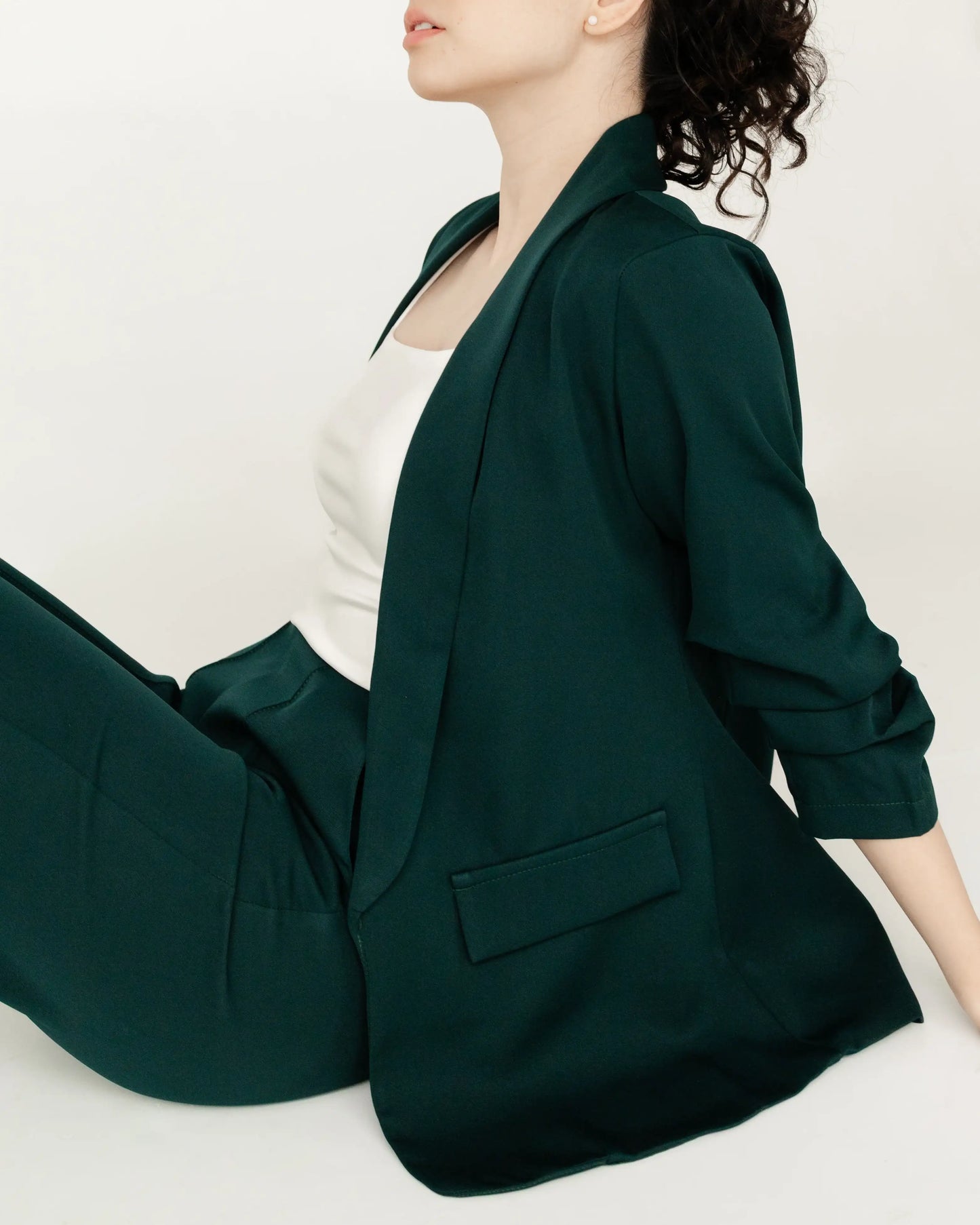 Mujer sentada con blazer verde oscuro y blusa blanca, estilo moderno y elegante