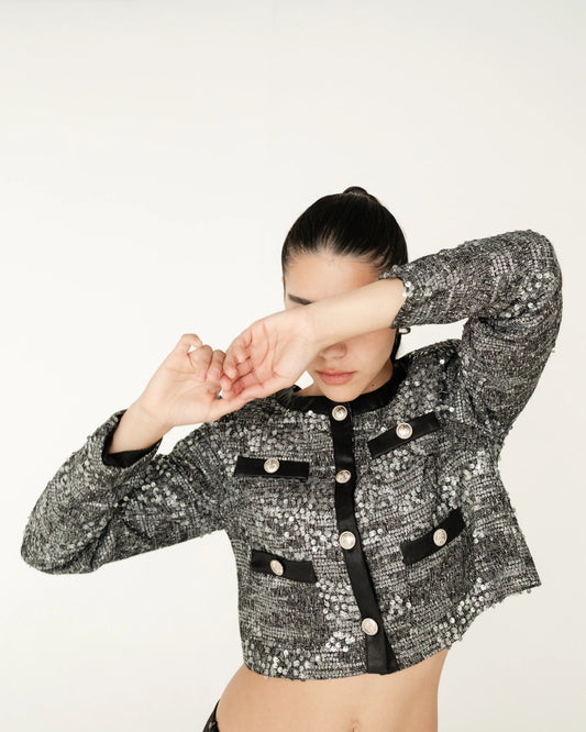 Mujer con chaqueta corta de lentejuelas gris y detalles negros, moda elegante