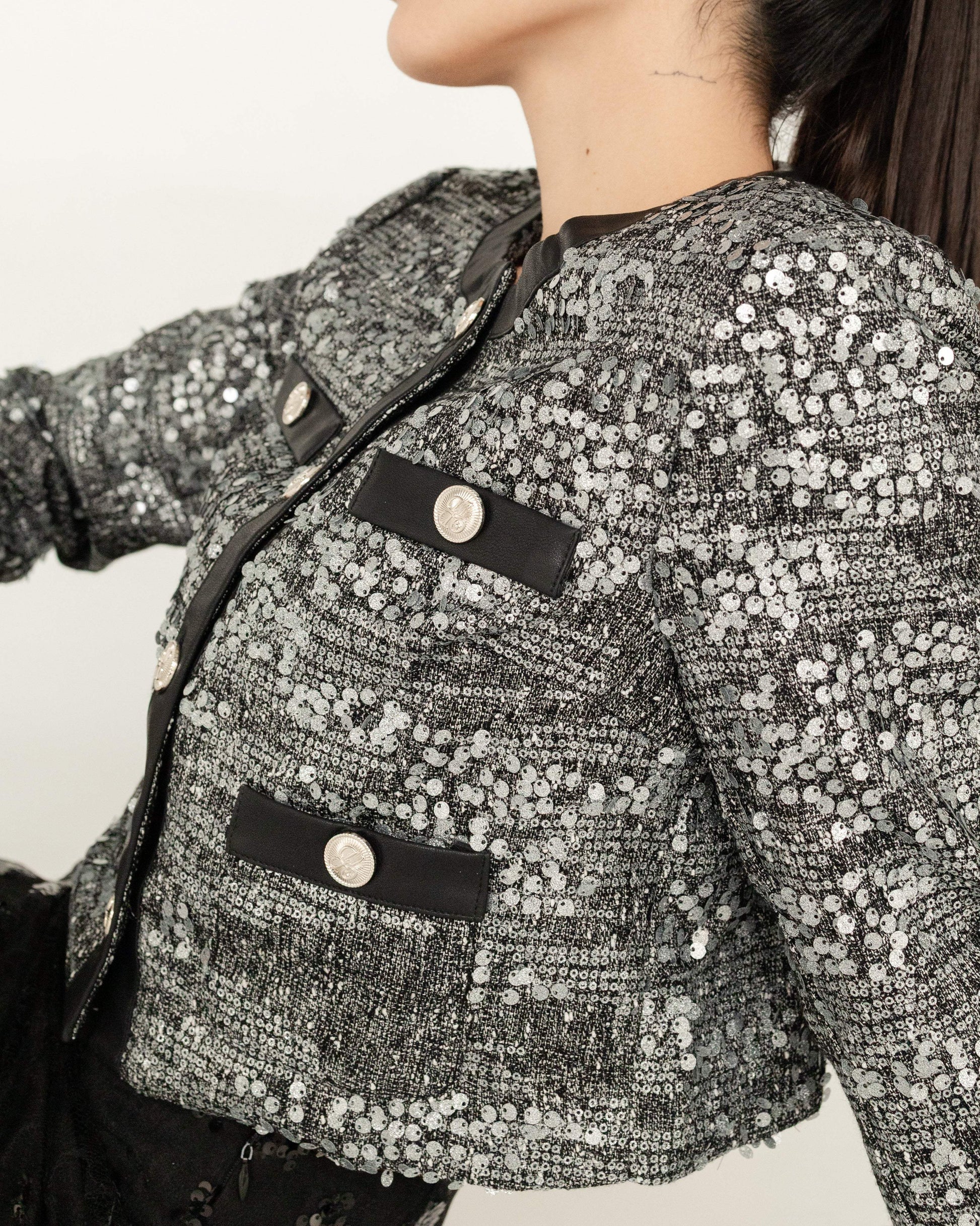 Saco corto de mujer con lentejuelas plateadas y botones decorativos, estilo elegante.