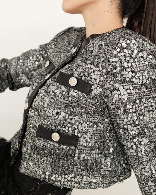 Saco corto de mujer con lentejuelas plateadas y botones decorativos, estilo elegante.