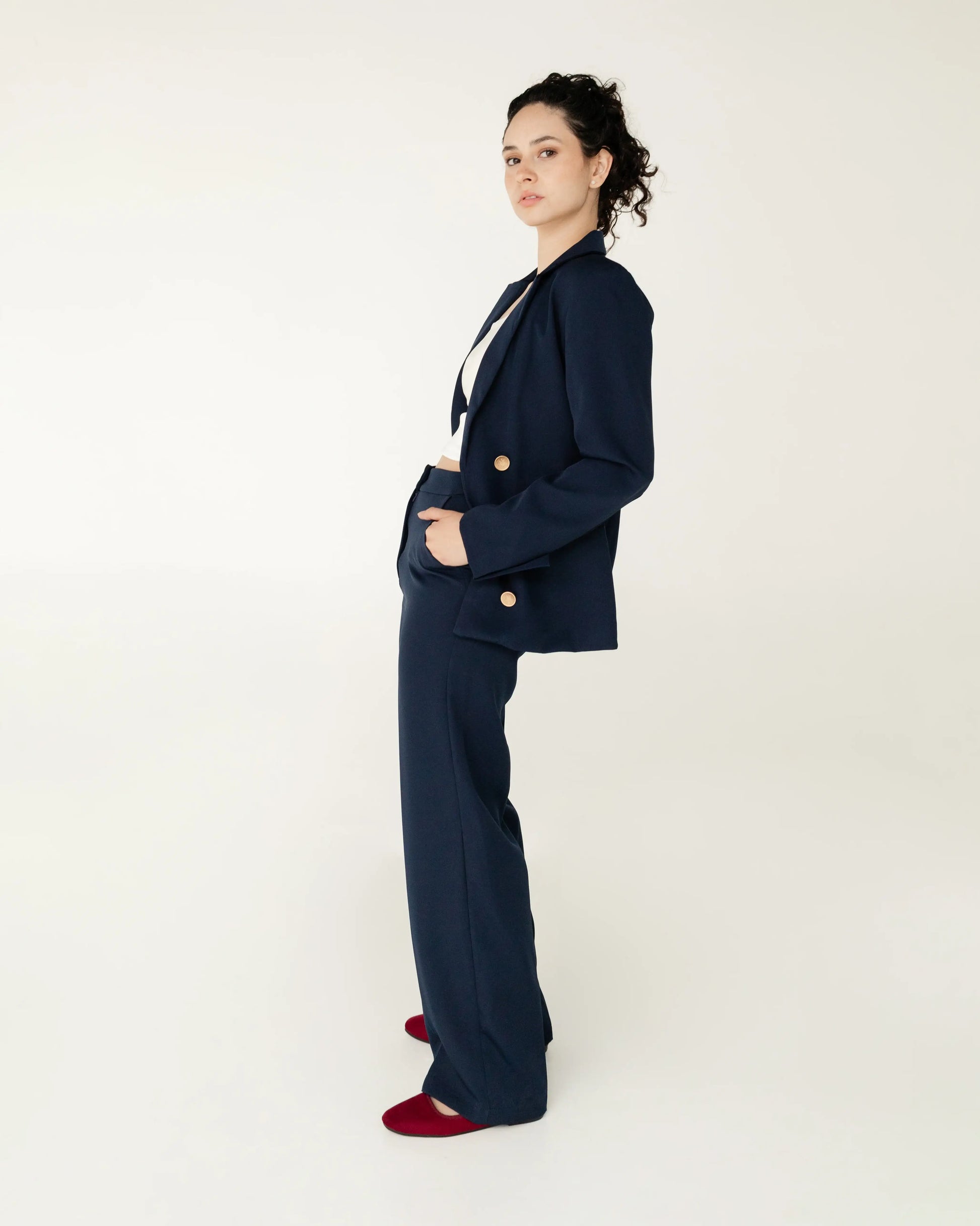 Mujer con traje sastre azul marino, top blanco y zapatos rojos en fondo neutro, estilo moderno