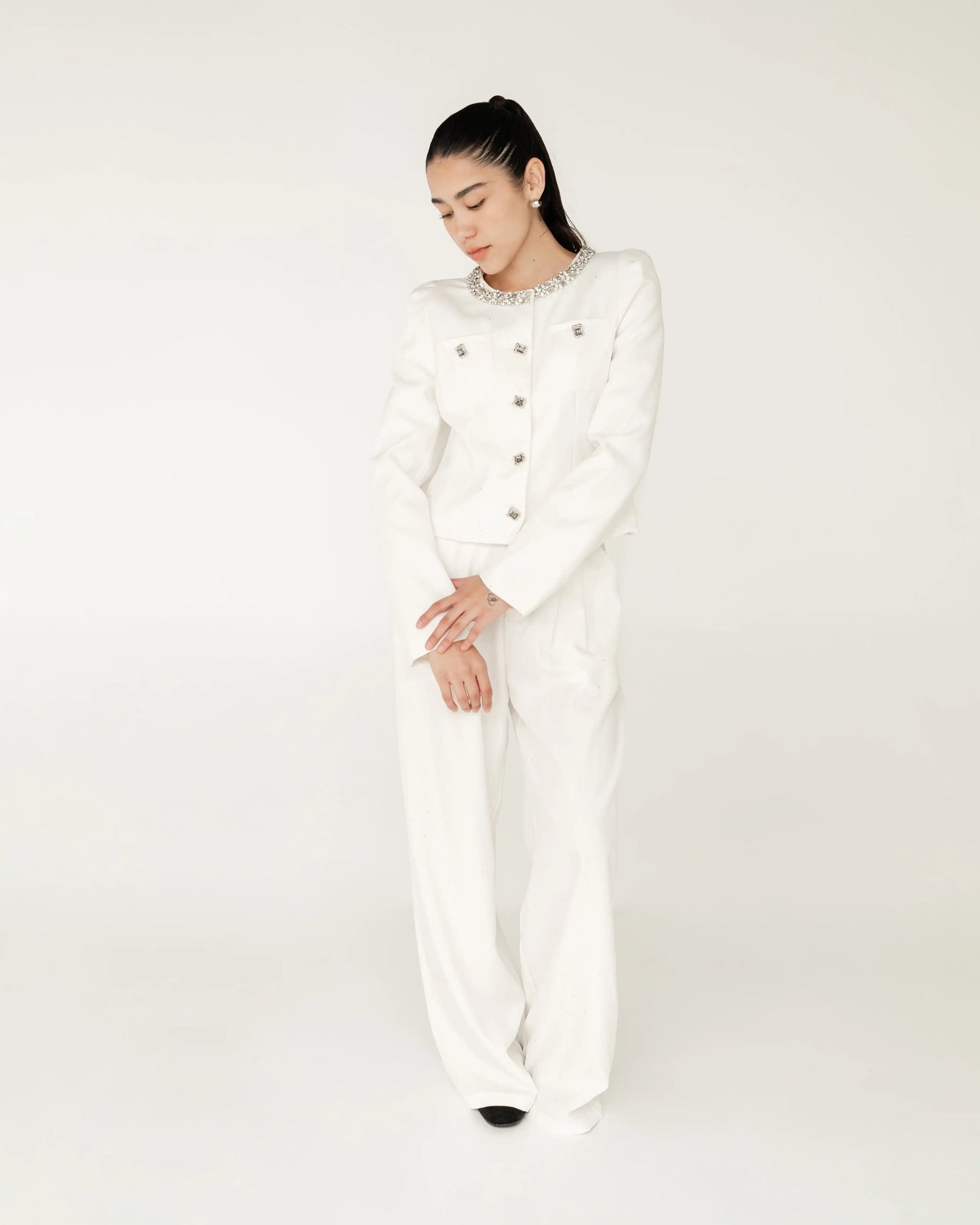 Mujer con traje blanco elegante, saco con botones y cuello decorado, fondo neutro