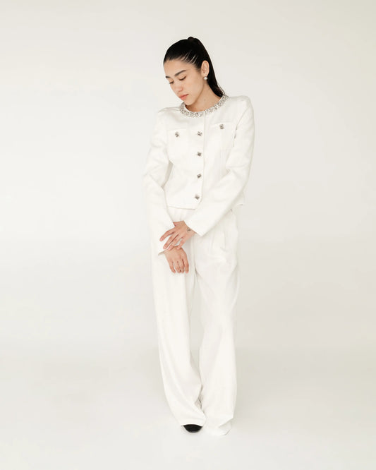 Mujer con traje blanco elegante, saco con botones y cuello decorado, fondo neutro