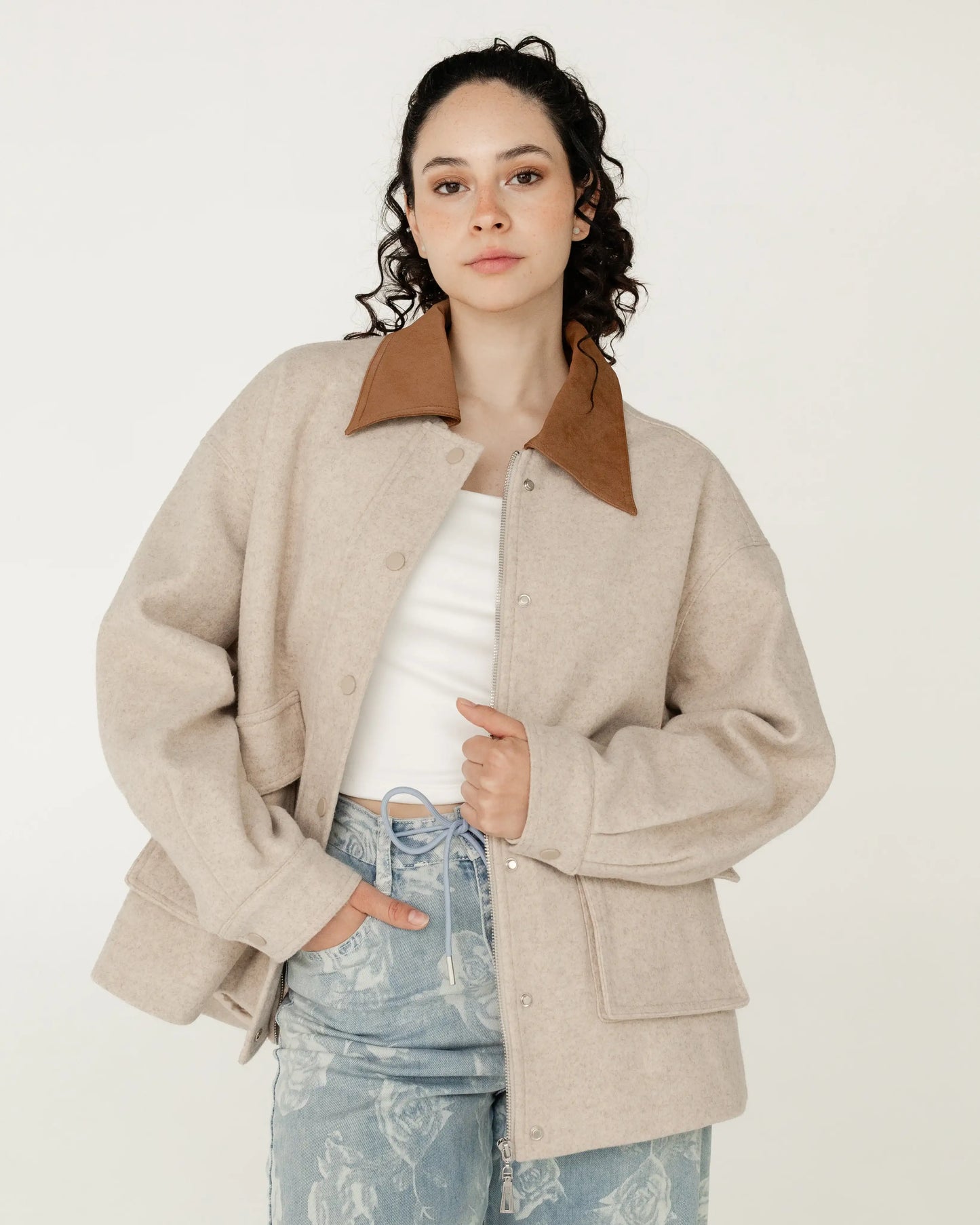 Mujer con chaqueta beige de lana y cuello café, jeans con estampado floral, estilo casual moderno