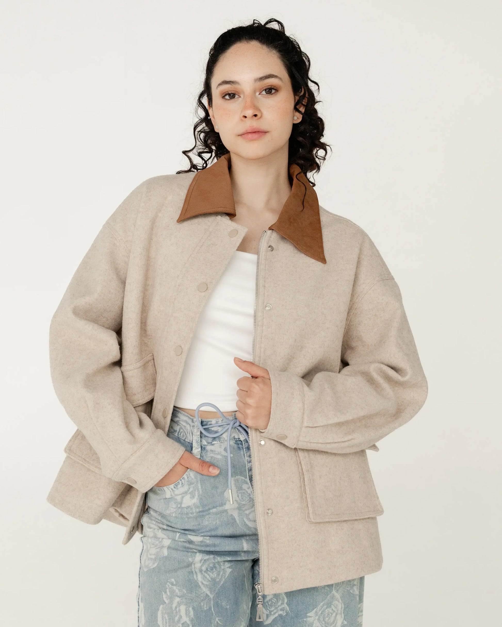Mujer con chaqueta beige de lana y cuello café, jeans con estampado floral, estilo casual moderno