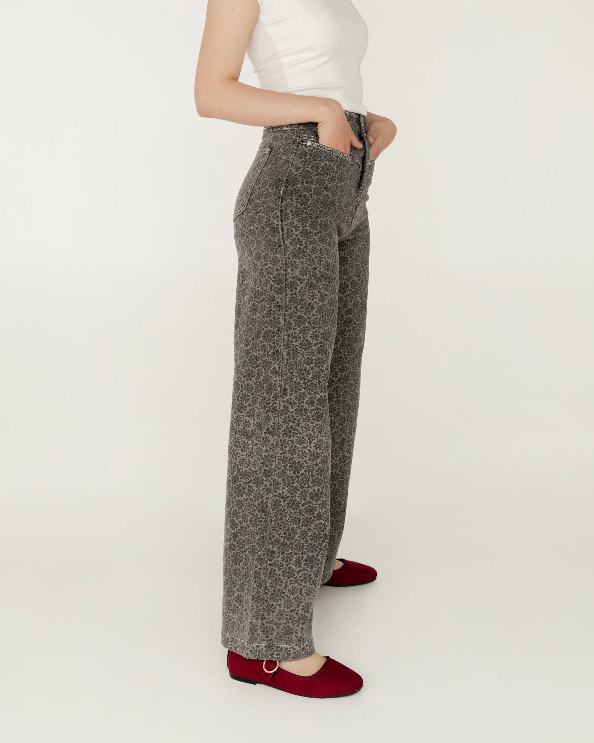 Pantalón gris de tiro alto con estampado floral, mujer de perfil, blusa blanca y zapatos rojos
