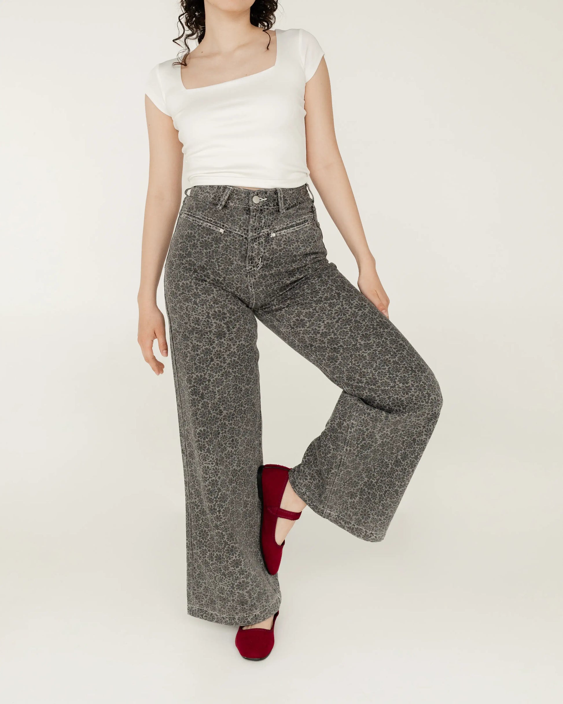 Mujer con jeans grises estampados, blusa blanca ajustada y flats rojos, moda casual.