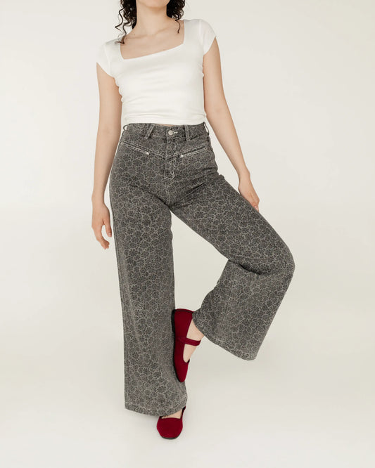 Mujer con jeans grises estampados, blusa blanca ajustada y flats rojos, moda casual.