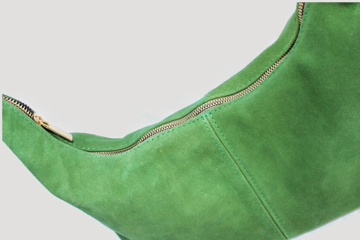 Bolso verde de gamuza con cierre metálico dorado sobre fondo claro