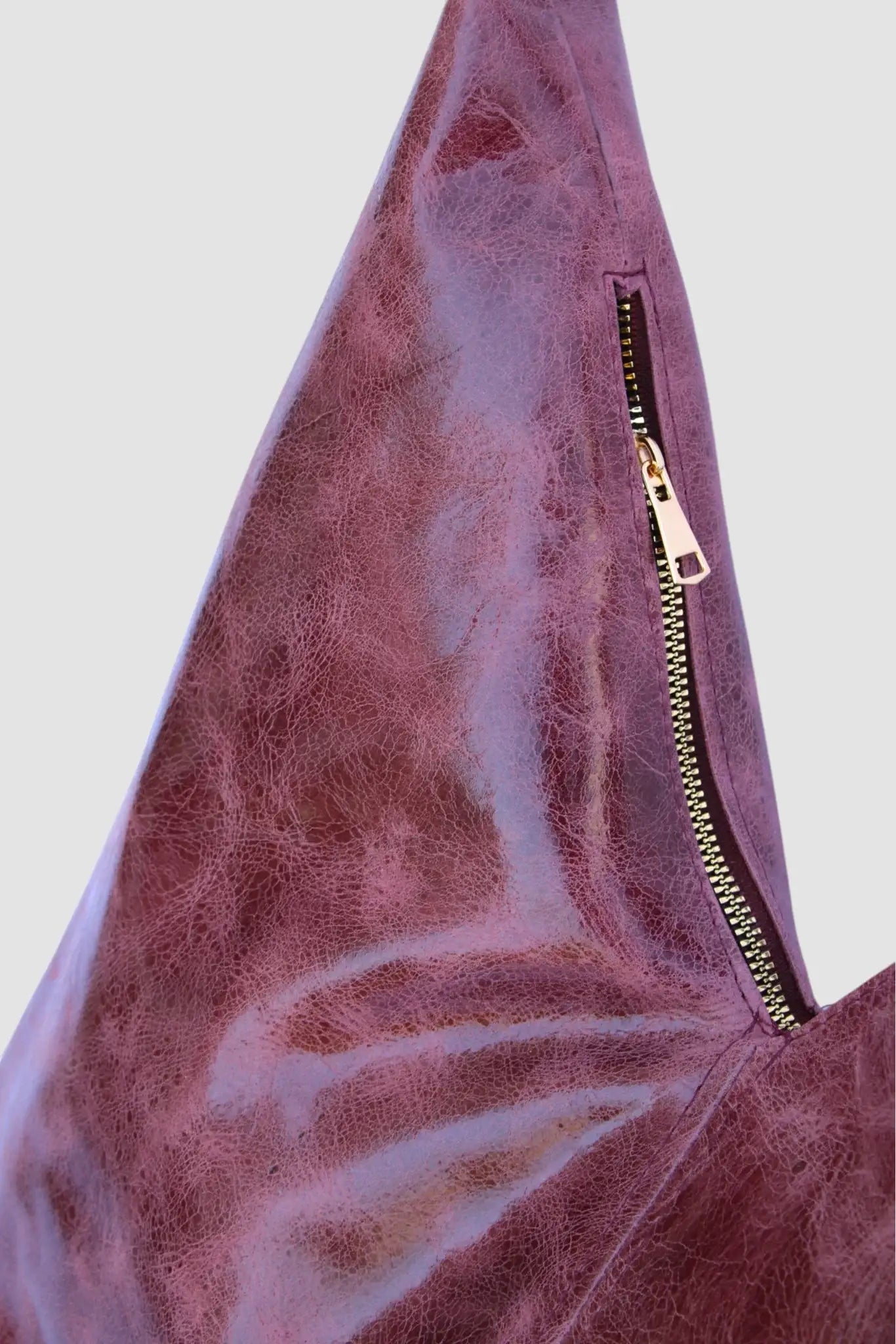 Bolso triangular de piel morada con cierre metálico visible, textura brillante